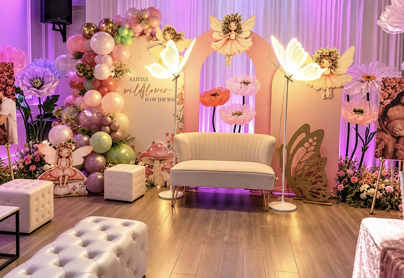 Colorful fairy baby shower with a pastel balloon garland, floral backdrop and cream loveseat